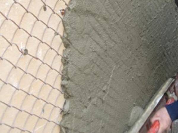 A man is plastering to a wall using chain link fence as support mesh