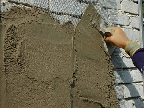 A trowel in a man’s hand is plastering on a wall with expanded metal as reinforcing mesh