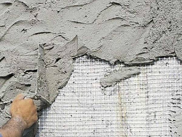 A man is plastering putty to a wall with fiberglass mesh as reinforcing layer.